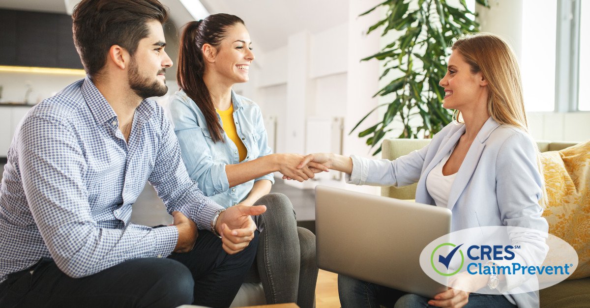 female real estate agent with laptop sitting on a couch shaking hands with a couple